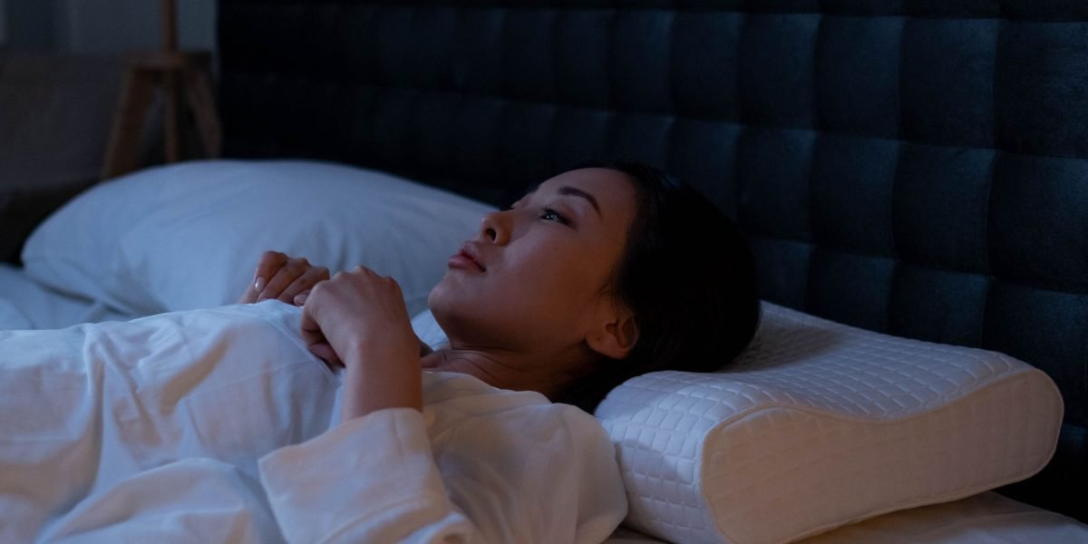 A person lying in bed with eyes closed but visibly restless, reflecting common struggles with sleep onset anxiety.
